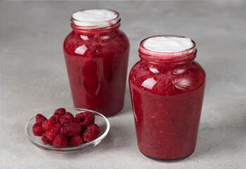 Fresh raspberries mixed with sugar in two glass jars on gray table - obrazy, fototapety, plakaty