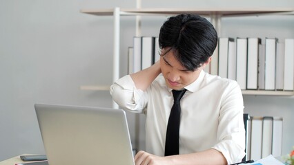 Exhausted young asian male worker suffer from strain muscles, neck pain while working on laptop at office. Tired stressed man having neck pain. Office Syndrome concept