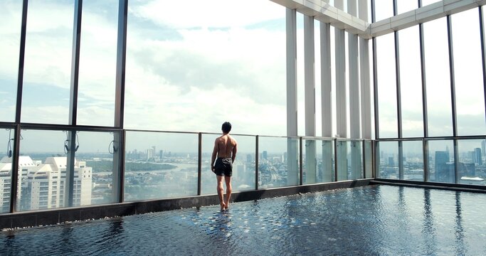 Back view of young man standing at swimming pool looking at beautiful view and blue sky in daytime