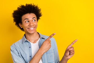 Photo of excited dreamy man wear jeans shirt pointing two fingers looking empty space isolated yellow color background