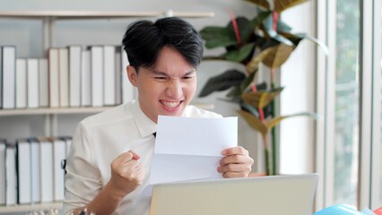 Young Asian man received great news highest mark successfully pass exams or test. Asian man Read paper notice with feels happy excited, celebrate university admission