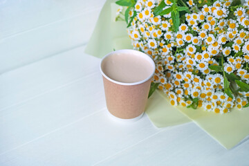 Cardboard cup with coffee and a bouquet of delicate rmoashki on a light background