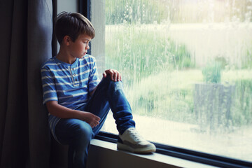 Boy child, rain and sad by window with thinking, mental health and space for mockup in home. Male kid, raining and think by glass with depression, mock up or bored with problem, winter or frustration