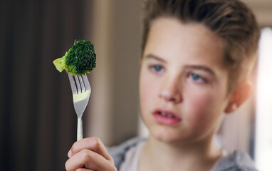 Disgust, food and refuse with child and broccoli for nutrition, health and cooking. Sad, angry and dinner with boy and green vegetable on fork at home for eating problem, frustrated and dislike