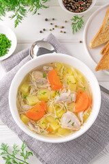 Chicken soup with noodles and vegetables in white bowl on a wooden background.