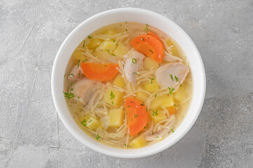 Chicken soup with noodles and vegetables in white bowl on a gray concrete background.