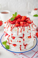 Pavlova layered cake with fresh strawberries, sauce and whipped cream on a white wooden background. Summer beautiful cake. Selective focus.