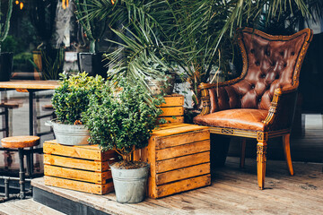 Cozy outdoor cafe exterior with armchair, wooden crates and plants in buckets