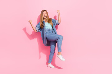 Full body photo of pretty young teenager girl raise fists celebrate lottery wear trendy jeans outfit isolated on pink color background