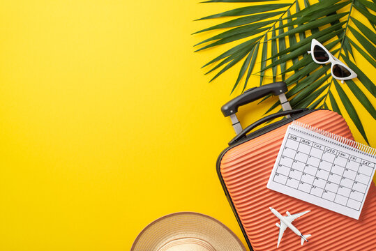 Summer vacation concept. Overhead view photo of suitcase with airplane model and calendar on it with by palm leaves, sunglasses and straw hat on isolated bright yellow background with copy-space - Powered by Adobe