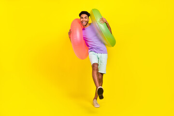 Full body photo of young man funky dancing pool party have fun inflatable circles holidays weekend isolated on yellow color background