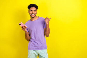 Fototapeta premium Photo of handsome blogger guy hold smart phone look indicate finger empty space isolated on yellow color background