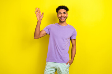 Photo of attractive excited man wear violet t-shirt smiling waving arm hello isolated yellow color background © deagreez
