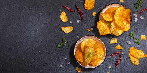 Bowls of homemade potato chips served with chili, parsley, seal salt on black stone background