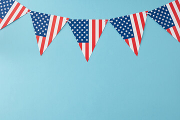 Idea for patriotic festivities on 4th of July. Top view flat lay of american triangular flag bunting on pastel blue background with empty space for text or advert