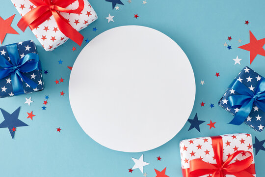American Independence Day gift themes. Top view flat lay of gift boxes in national colors, patriotic sparkles on light blue background with blank circle for greeting or promotion text
