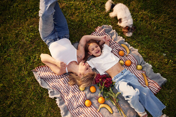 On the blanket with oranges and bananas. Woman with her little daughter are on the summer field...