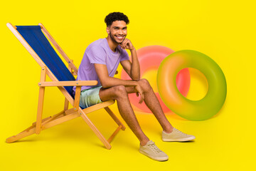 Full body photo of young man touch chin sitting concentrated sunbed posing for magazine travel agency isolated on yellow color background