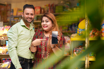 Indian couple showing smartphone screen at grocery shop.