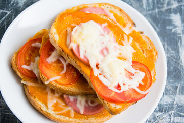 Delicious hot sandwiches with cheese, sausage and tomato, close-up, on a white plate, flatlay