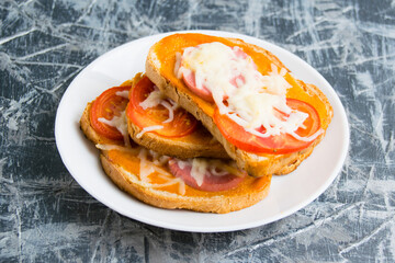 Delicious hot sandwiches with sausage, cheese and hot sauce, on white bread, on a gray plate
