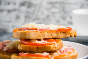 Delicious breakfast, hot sandwiches with tomato, cheese and sausage on a white plate and a cup of coffee on a gray background