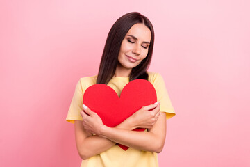 Photo of adorable sweet woman dressed yellow t-shirt closed eyes cuddling red heart isolated pink color background