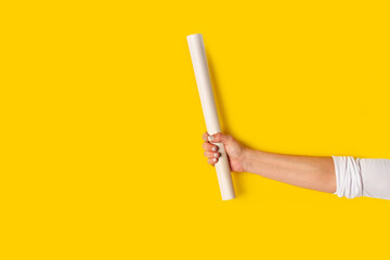 Mano de mujer sosteniendo un rollo de papel sobre un fondo amarillo brillante liso y aislado. Vista de frente y de cerca. Copy space