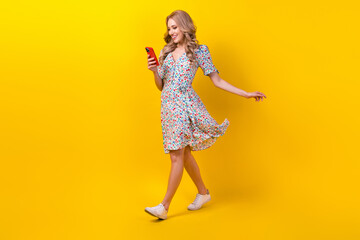 Full length photo of cute carefree woman dressed flower print sarafan typing sms modern device isolated yellow color background