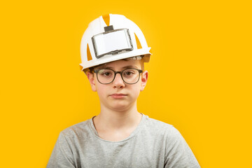 Portrait of teenage boy wearing glasses and protective white helmet isolated on yellow background. Child is like builder or an engineer.