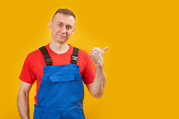 Handsome male foreman engineer wearing blue overalls and points with his finger to the side. Studio...