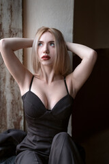 Attractive young blonde woman wears black top with deep sweetheart neckline with her hands behind head. Girl with seductive figure.