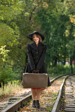 Woman in black hat and coat holds retro valise. Madame in clothes of 30-40s style mysteriously. Vertical frame