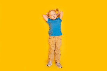 Little girl with two ponytails wears blue T-shirt and yellow pants. Child lying on bright yellow background. Top view