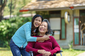 Naklejka premium Asian senior woman in wheelchair with happy daughter. Family relationship retired woman sitting on wheelchair in the park age care at retirement home.