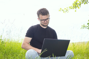Remote work with a computer. A man in nature with a computer. Sit with a computer outdoors