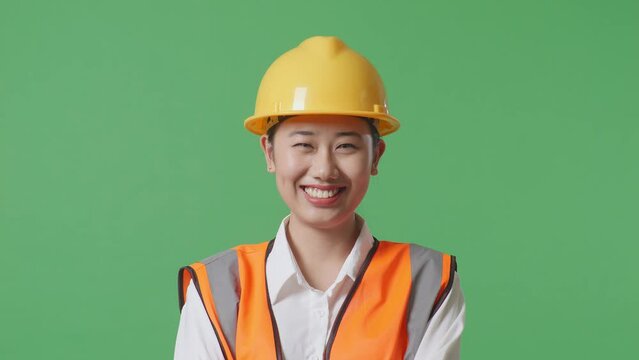 Close Up Of Asian Female Engineer With Safety Helmet Crossing Her Arms And Smiling To Camera While Standing In The Green Screen Background Studio
