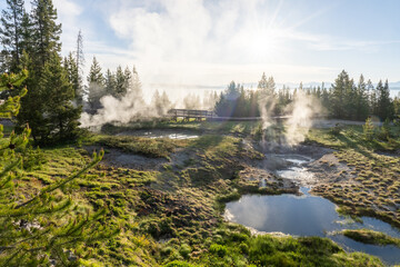 Clouds of steam are rising from pools of hot water illuminated by intense low angle sunlight, Twin...