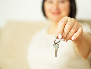 Close up of an attractive cheerful middle aged woman holding a key of her new house in her hand.