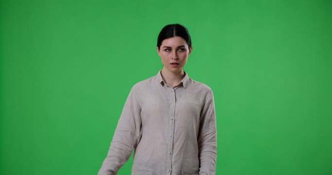 Caucasian woman standing against a green screen background, looking bored and making a blah blah blah hand gesture, as if expressing her disinterest in what's being said.