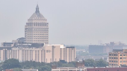 Obraz premium Poor air quality in Rochester NY caused by Canadian wildfire smoke over the city skyline dense around downtown office buildings due to climate change conditions in Canada
