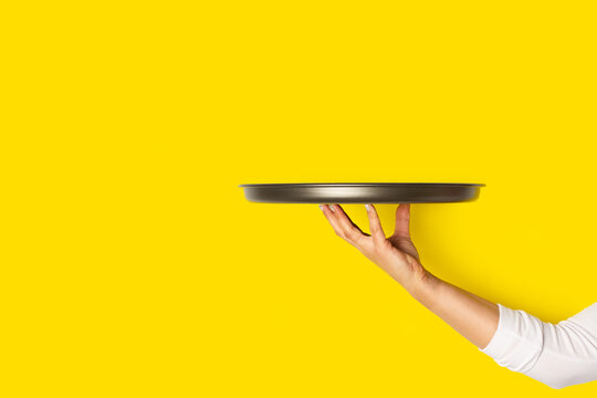 Mano de mujer sosteniendo una bandeja de metal sobre un fondo amarillo brillante liso y aislado. Vista de frente y de cerca. Copy space