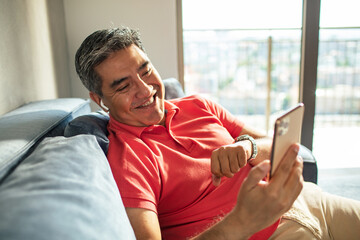 MIddle aged latin man using a smart phone on a couch at home
