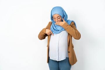 Shocked Young beautiful pregnant muslim woman wearing hijab over white background look surprisedly...