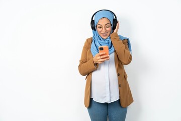 Happy Young beautiful pregnant muslim woman wearing hijab over white background feels good while focused in screen of smartphone. People, technology, lifestyle