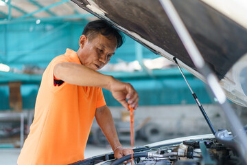 Senior Asian man checking or measuring a vehicle oil engine or engine lubricant level by using oil...
