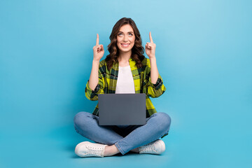 Full length portrait of cheerful pretty person sit floor use netbook look direct fingers up empty space isolated on blue color background