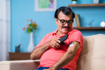 Elderly senior man checking glucose level by tapping smartphone to monitoring sensor at home -...