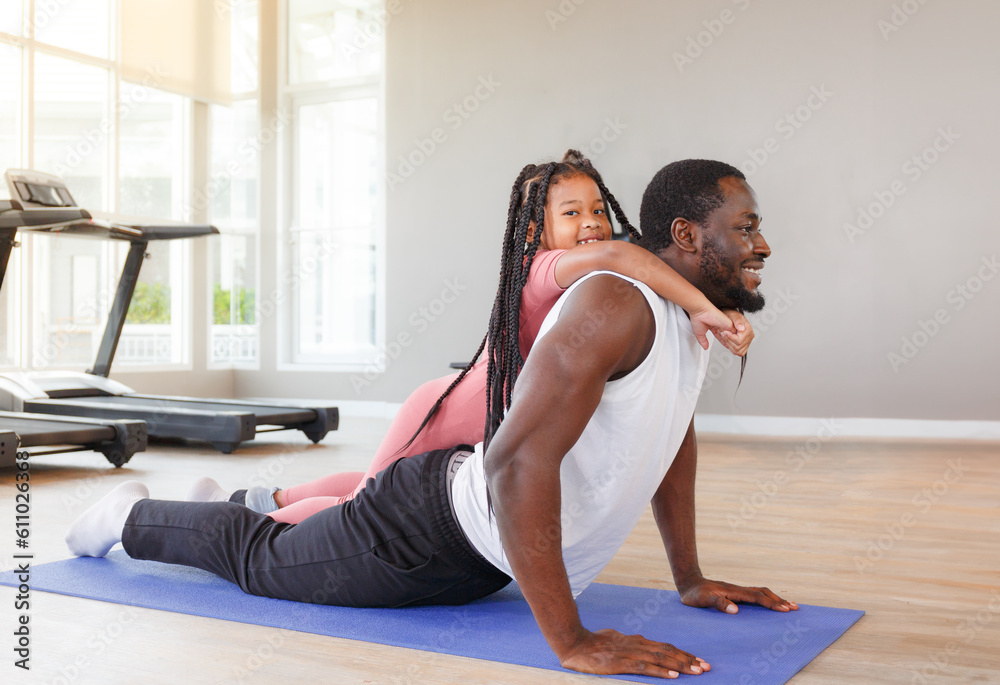 Wall mural Father doing yoga with cute daughter, beginner doing simple exercise on purple background in gym.