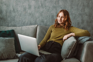 Serious woman using laptop checking email news online sitting on sofa, searching for friends in internet social networks or working on computer, writing blog or watching webinar, studying at home